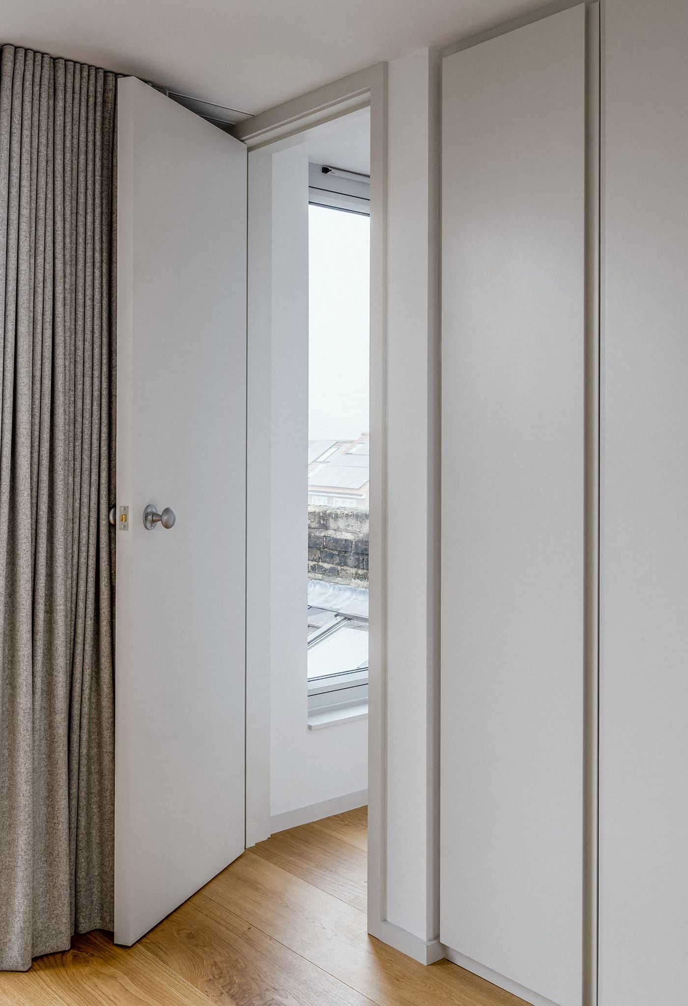 Internal view looking into at the built in wardrobes within the rear dormer extension with light grey joinery and lightweight curtains at Northbrook Road designed by From Works.